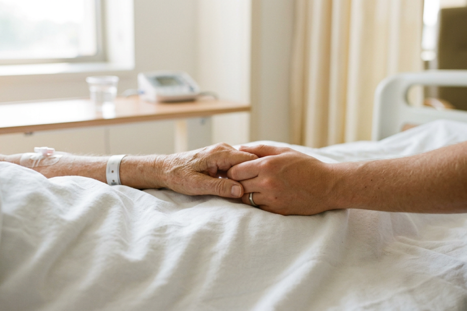 Duas mãos entrelaçadas sobre o lençol branco de uma cama de hospital